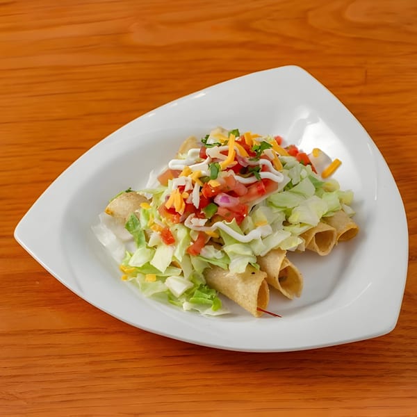 Aztk's taquitos topped with shredded lettuce, diced tomatoes, cheese, and sour cream on a white plate.