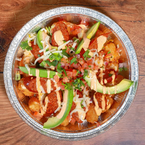 Aztk Mexican tater tots with chorizo, avocado, pico de gallo, and sauce in a foil container.