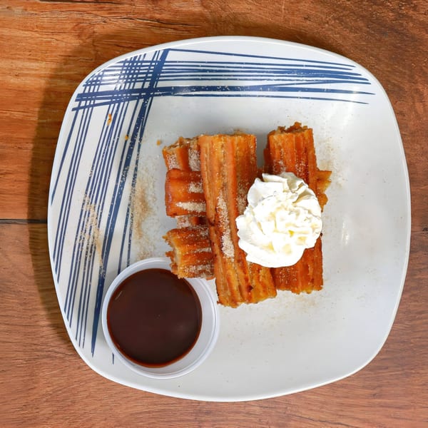 Aztk churros with whipped cream and chocolate dipping sauce on a white plate with blue stripes.