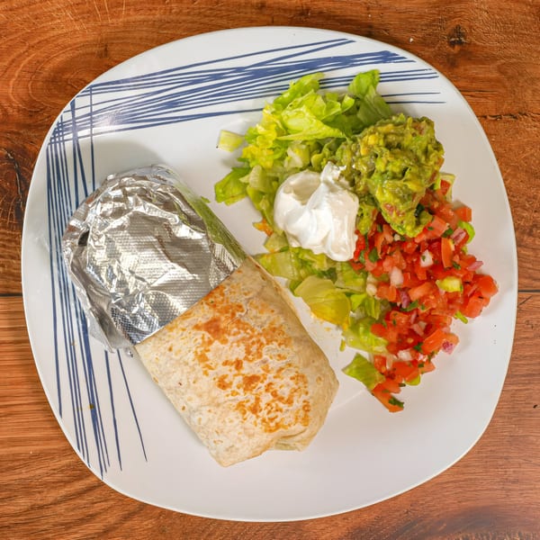 Aztk burrito with foil, lettuce, guacamole, sour cream, and pico de gallo on a white plate.