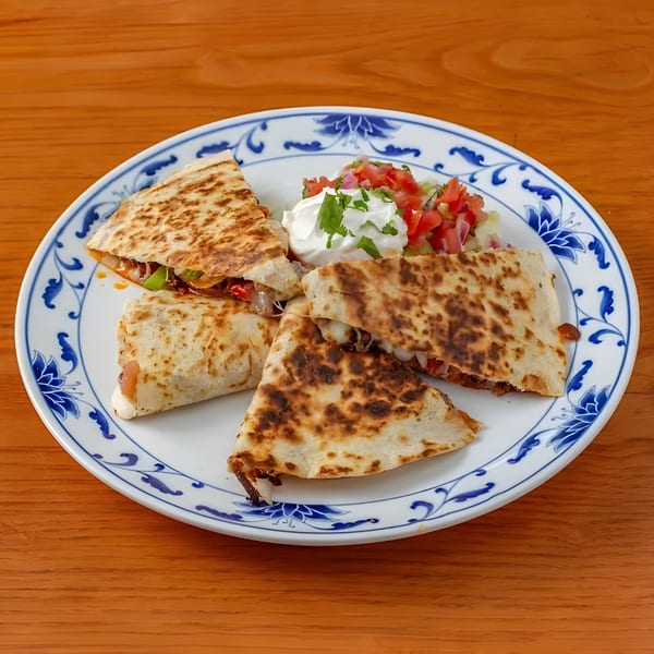Four quesadilla wedges with pico de gallo and sour cream on a white and blue patterned plate.